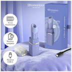 Womanizer Beauty lilas sur un lit, avec son coffret, son capuchon et les indications de recharge USB-C.