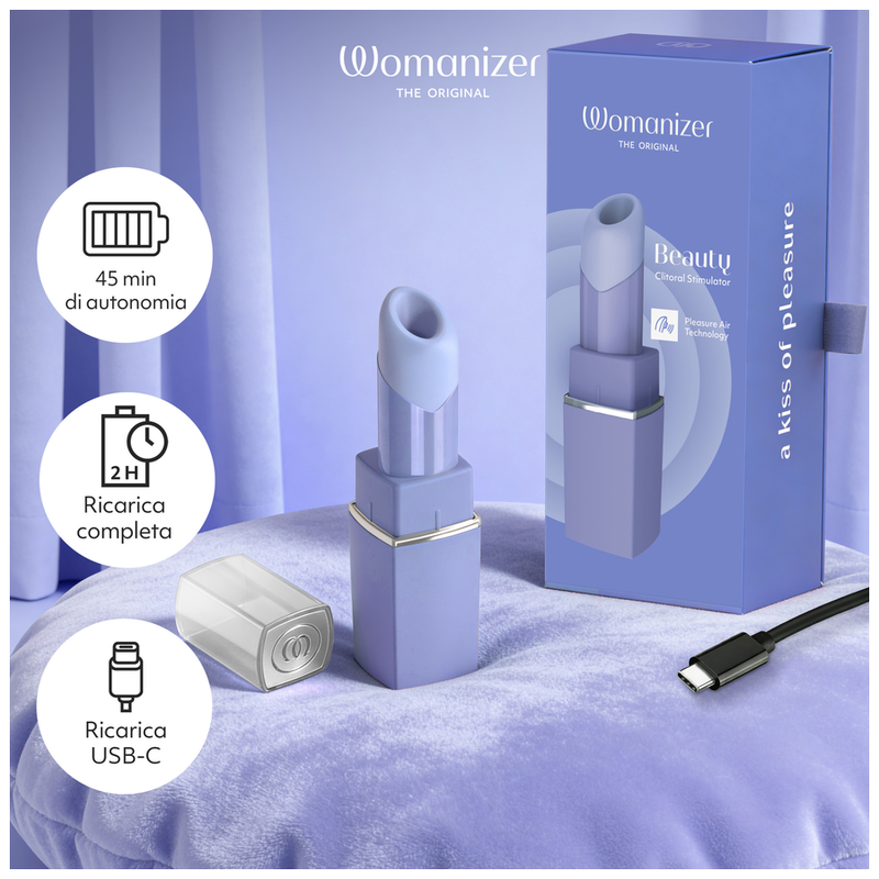 Womanizer Beauty lilas sur un lit, avec son coffret, son capuchon et les indications de recharge USB-C.