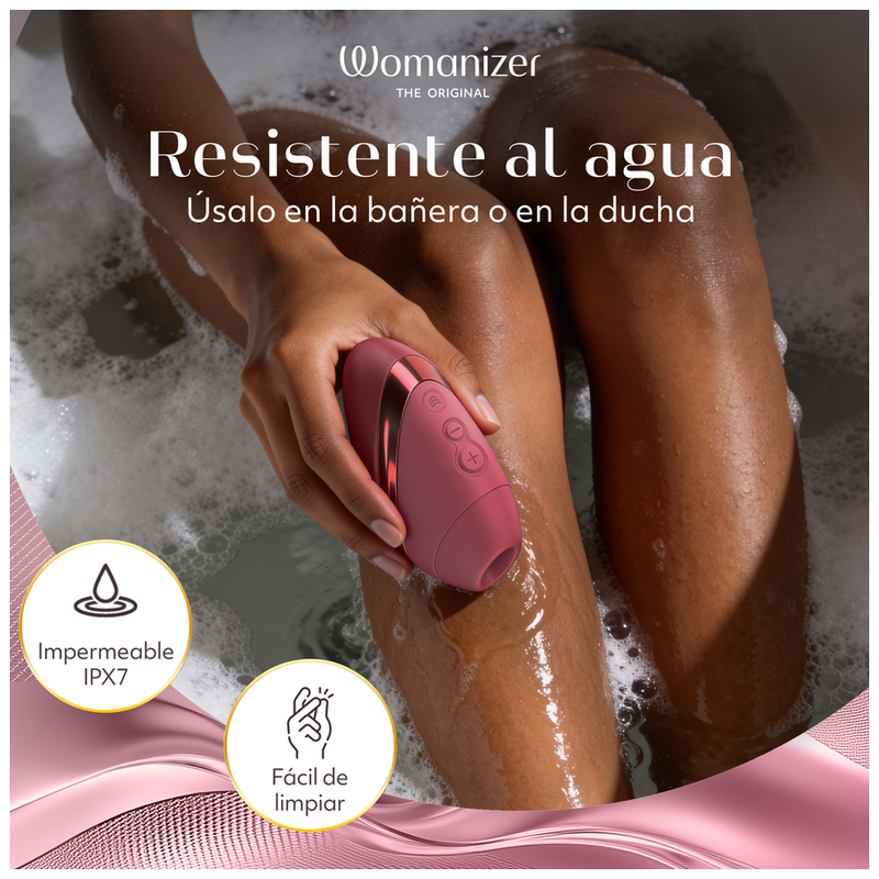 Womanizer Next Liberty Bordeaux tenu au-dessus d’un bain moussant, avec une indication d’étanchéité IPX7.