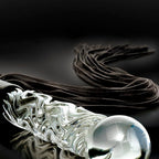 Detail artistique de la poignee en verre transparent du fouet posee parmi ses lanieres souples, manche souffle a la main au rendu lumineux et lisse.
