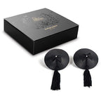 Coffret noir Bijoux Indiscrets avec les cache-tétons à pompons et nœud posés devant, accessoire de poitrine burlesque adhésif et réutilisable pour habiller la peau.