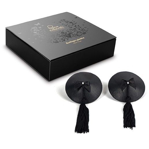 Coffret noir Bijoux Indiscrets avec les cache-tétons à pompons et nœud posés devant, accessoire de poitrine burlesque adhésif et réutilisable pour habiller la peau.