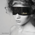 Modèle portant le masque satin noir Shhh sur les yeux, visage et épaules nues en noir et blanc, mise en scène sensuelle du bandeau de privation visuelle Bijoux Indiscrets.
