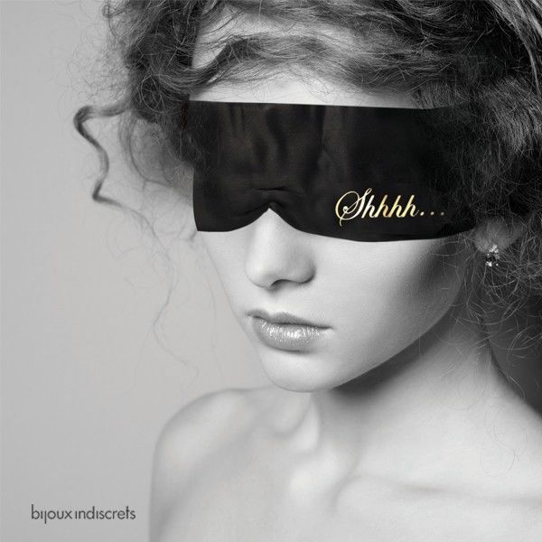 Modèle portant le masque satin noir Shhh sur les yeux, visage et épaules nues en noir et blanc, mise en scène sensuelle du bandeau de privation visuelle Bijoux Indiscrets.