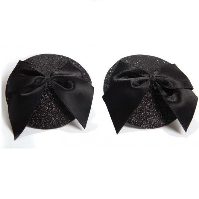 Paire de cache-tétons burlesques noirs à paillettes ornés d'un nœud satin vus de face, accessoire de poitrine adhésif et réutilisable Bijoux Indiscrets.