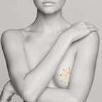 Modele bras croises sur la poitrine portant un tatouage temporaire Mimi dore Bijoux Indiscrets, mise en scene metallisee de la decoration corporelle sur la peau.