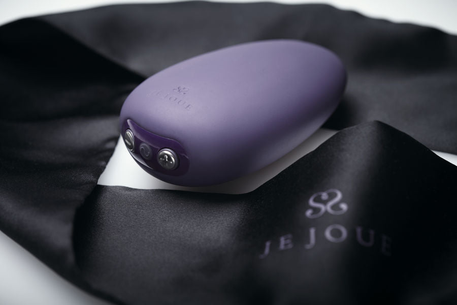 Vibrateur Mimi Soft violet déposé sur un long ruban de satin noir signé Je Joue, plan rapproché chaleureux, silicone mat élégant sans contenu explicite.