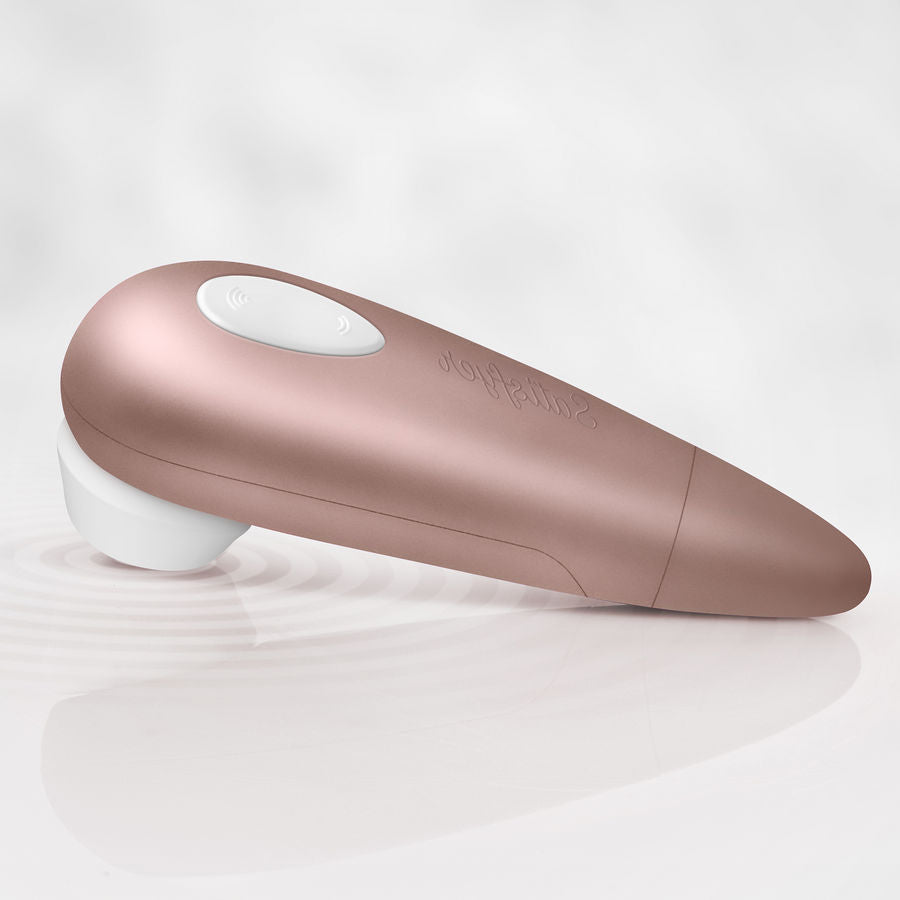 Stimulateur clitoridien dore Satisfyer couche sur une eau ridee, embout silicone blanc et bouton goutte, ambiance etanche, ondes de pression sans contact direct sur pile.