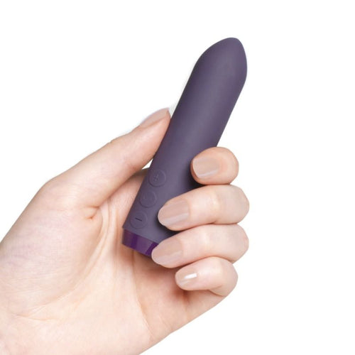 Main tenant le mini bullet violet debout entre les doigts, démonstration de format de poche, silicone mat à commandes moulées, objet discret signé Je Joue.