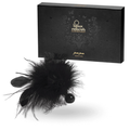 Plumeau sensoriel Pom Pom en plumes noires synthétiques posé devant sa boîte noire Bijoux Indiscrets, accessoire ultra-léger pour des caresses érogènes tout en douceur.