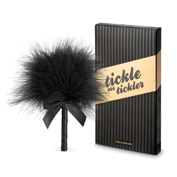 Plumeau sensoriel noir posé près de sa boîte Tickle Me Tickler noire et dorée, accessoire BDSM léger Bijoux Indiscrets pour caresser les zones sensibles du corps.