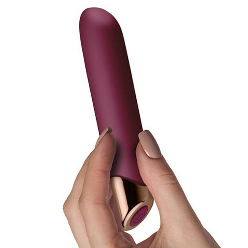 Vibromasseur point G Chaiamo bordeaux tenu entre les doigts d'une main, pointe effilée et base dorée, illustrant le format de ce stimulateur silicone velouté.