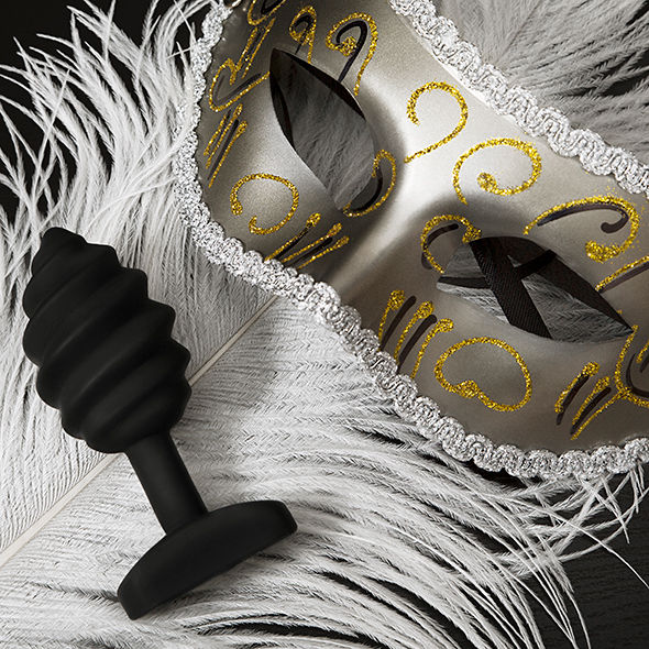 Plug anal vibrant G-Vibe en silicone noir presente sur des plumes blanches a cote d'un masque venitien dore, ambiance feutree et raffinee pour le jeu anal.
