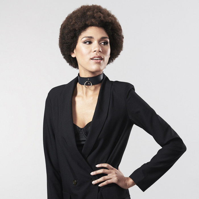 Modele en veste noire portant le collier ras de cou a anneau Bijoux Indiscrets, accessoire BDSM vegan reglable, mise en scene audacieuse mode et soft bondage.