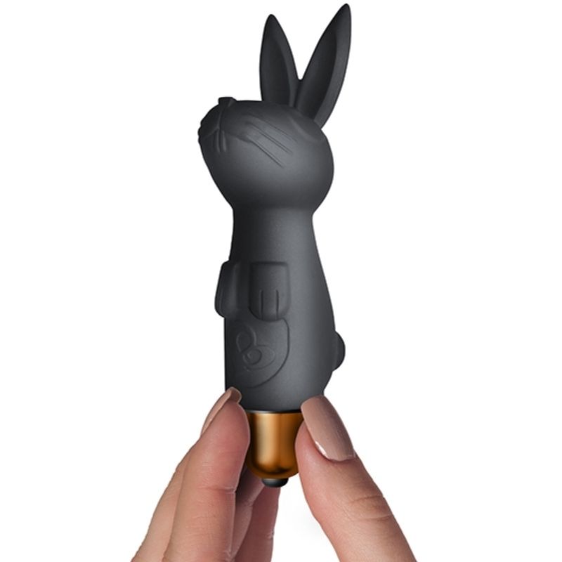 Main féminine tenant le mini vibromasseur lapin noir à oreilles entre deux doigts, capsule dorée à la base, illustrant son gabarit compact en silicone.