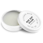 Baume clitoridien Bad Day Killer Bijoux Indiscrets, pot blanc ouvert laissant voir la texture cremeuse, couvercle pose a cote, cosmetique chauffant 8 g sur fond blanc