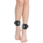 Menottes de cheville Darkness en cuir PVC noir portees, presentees sur des jambes pour illustrer le maintien des chevilles dans un jeu de bondage soft.