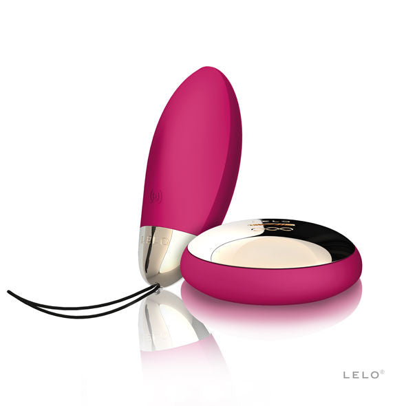 Œuf vibrant Lyla 2 de Lelo rose dressé derrière sa télécommande dorée posée à plat, embout chromé et dragonne, set de stimulation interne sans fil.