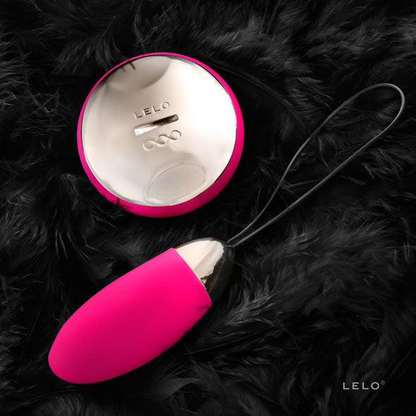 Œuf vibrant Lyla 2 de Lelo rose relié à sa télécommande dorée par son cordon, posé sur des plumes noires, vue rapprochée du stimulateur télécommandé.