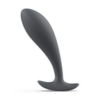 Plug prostatique fin anthracite à tête effilée et col mince, base plate évasée stabilisante. Profil élancé en silicone lisse posé sur fond blanc, contour épuré sans anatomie.