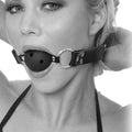Gros plan en noir et blanc du baillon boule respirant porte, boule percee de trous et sangle en cuir a anneaux ajustee autour du visage.