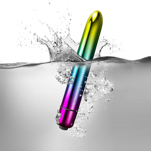 Balle vibrante Prism aux reflets arc-en-ciel plongeant dans l'eau avec éclaboussures, illustrant l'étanchéité IPX7, surface métallisée brillante non anatomique.